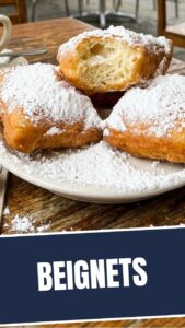 A pile of freshly fried New Orleans style beignets, dusted generously with powdered sugar, ready to be served.